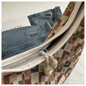 Macro detail of geometric woven bag featuring a metal zipper and pearl bead charm puller