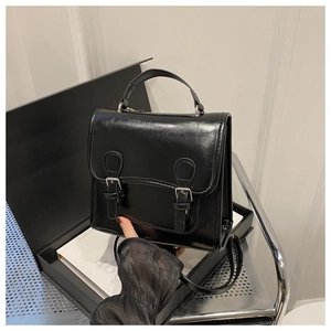 Close-up of black glossy faux leather handbag with dual adjustable buckle straps and handle