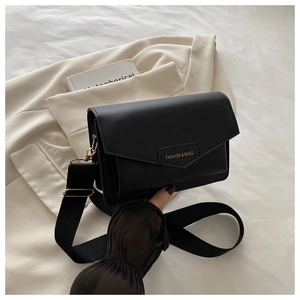 Close-up of matte black leather square bag with gold hardware and wide woven shoulder strap