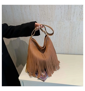 Detail of brown pebbled leather tote featuring long fringe tassels and golden metal grommets