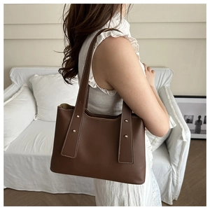 Detail of a brown tote bag with white stitching and metal studs on the wide shoulder strap