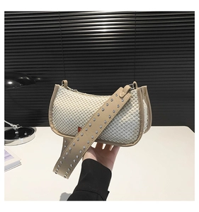 Detail of woven beige shoulder bag featuring a wide strap with silver round rivets