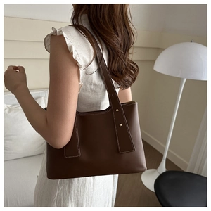 Detail of dark brown leather tote bag featuring white contrast stitching and gold rivets
