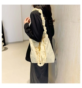 Close-up of cream shoulder bag with ruffled straps and pearl accents on fabric
