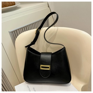 Detail of black faux leather bag with gold woven texture clasp on a beige chair