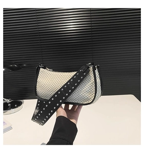 Detail of cream woven bag with wide black leather strap featuring silver studded rivets