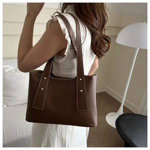 Close-up of a large dark brown tote bag featuring contrast stitching and gold rivets