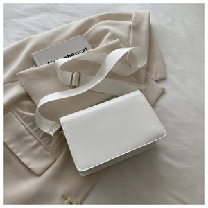 Detailed shot of a white faux leather crossbody bag with wide strap and gold hardware accents
