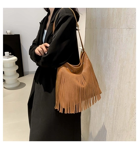 Detail of caramel leather shoulder bag featuring dense long tassels and metal eyelets