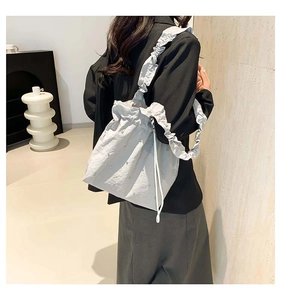 Close-up of ruffled shoulder strap and pearl embellishments on light grey bucket bag