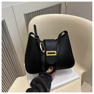Detail of minimalist black shoulder bag featuring polished gold buckle and adjustable strap