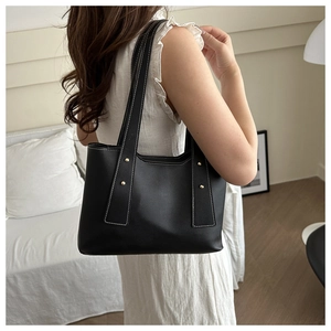 Detail of black PU leather tote bag with white contrast stitching and gold rivets