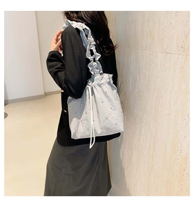 Detail of grey bucket bag showing ruffled strap and pearl embellishments on shoulder
