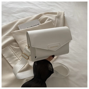 Detail of white square crossbody bag with gold hardware and wide fabric shoulder strap