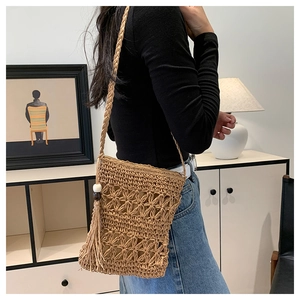Detail of hand-woven straw crossbody bag with hollow crochet patterns and tassels