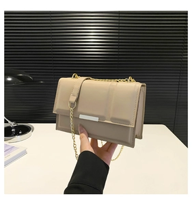 Detail view of a beige crossbody bag with gold chain strap held by a model on desk