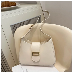 Detail of cream leather shoulder bag featuring a rectangular gold buckle on a white chair