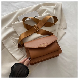 Close-up of brown PU crossbody bag with woven nylon strap on a beige blazer background