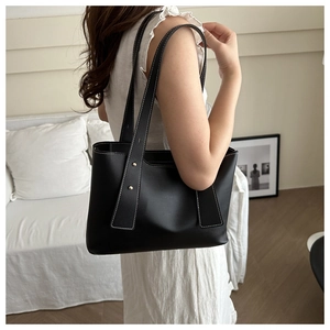 Detail of black bucket bag featuring white contrast stitching and gold metal studs