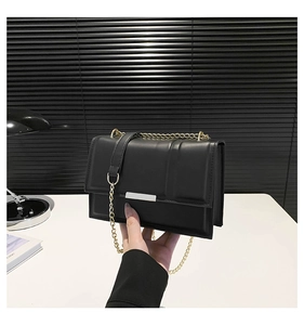 Detail of a black square bag with a silver metal bar and gold chain strap