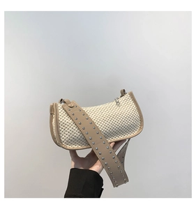 Close-up of beige woven straw tote bag featuring trendy wide strap with metal rivets