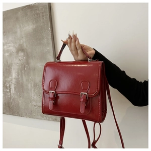 Detail of red glossy patent leather backpack showing flap closure and buckle straps
