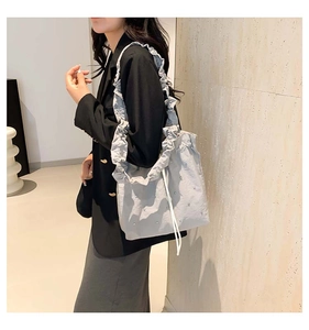 Light gray bucket bag with pearl accents and ruffled shoulder strap shown on model