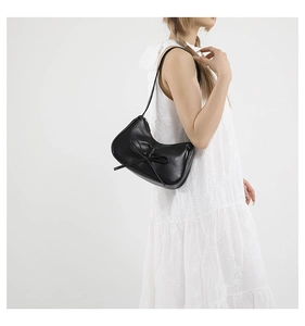 Détail du sac croissant noir avec nœud papillon porté sur une robe en dentelle