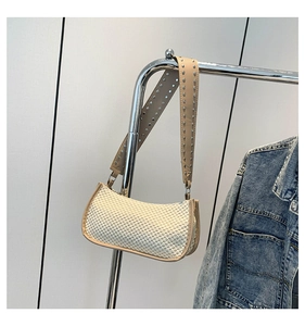 Close-up of woven straw baguette bag with silver rivets on a khaki leather strap