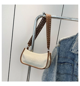 Detail of straw woven bag with brown PU leather trim and silver rivets on the wide strap