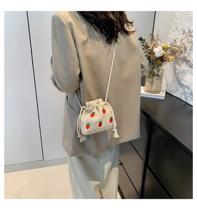 Detail of beige knitted bucket bag featuring red strawberry embroidery and drawstring closure