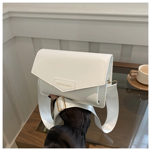 Detailed shot of white faux leather crossbody bag with wide nylon strap on a wooden table