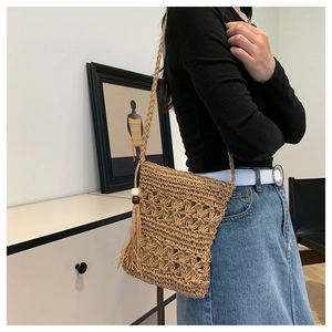 Detailed view of woven straw crossbody bag with floral cutouts and tassel accents