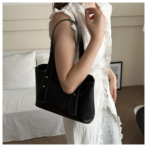 Detail of black leather tote bag with white stitching and gold studs on a shoulder strap