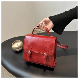 Detail of red glossy faux leather satchel with dual buckle straps and top handle