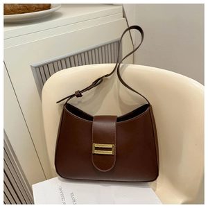 Close-up of a large dark brown leather tote bag with a golden buckle on a white chair