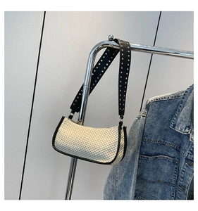 Detail of white woven bag featuring a black shoulder strap with silver metal rivets