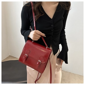 Model showcasing a deep red vintage satchel bag with a top handle and buckle details