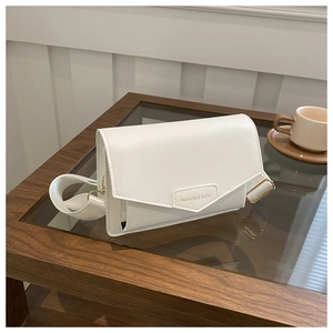 Close-up of white crossbody bag with gold hardware and wide fabric strap on a table