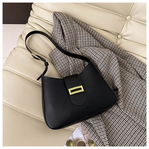 Detail of a black minimalist shoulder bag with a gold rectangular buckle on a white sofa