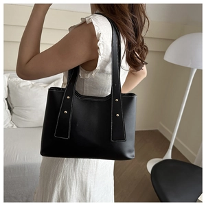 Detail of black leather tote bag with white contrast stitching and gold metal rivets