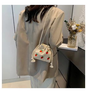 Close-up of straw woven bucket bag featuring red strawberry embroidery and drawstring