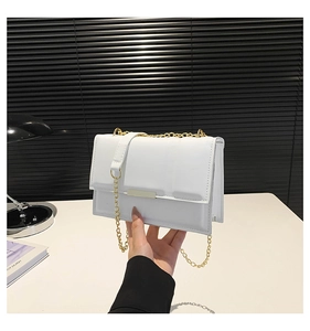 Close-up of white quilted leather flap bag with gold chain strap held by a hand