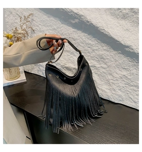Detail of black pebbled leather hobo bag featuring golden eyelets and long fringe tassels