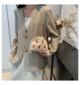 Detail of beige woven straw bucket bag featuring embroidered red strawberry patterns