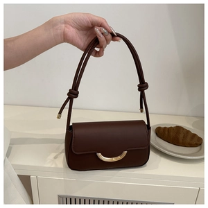 Détail du sac bandoulière en cuir marron avec boucle dorée et bandoulière à nœuds
