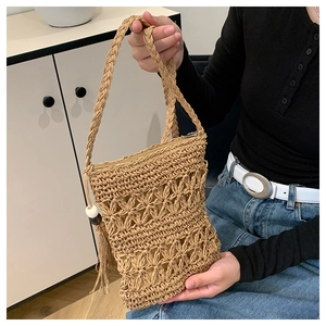 Detail of straw woven crossbody bag with hollow patterns, tassel, and braided strap