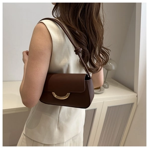 Détail d'un sac baguette en cuir marron foncé avec fermoir demi-lune doré porté à l'épaule