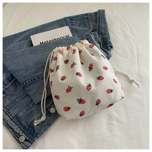 Gros plan du sac seau en velours à motif fraise avec cordon sur une veste en jean