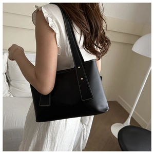 Detail of a black faux leather tote with white contrast stitching and gold rivets